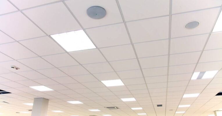Large white commercial space with white pillars showing LED panel lights stretching across the ceiling in rows.
